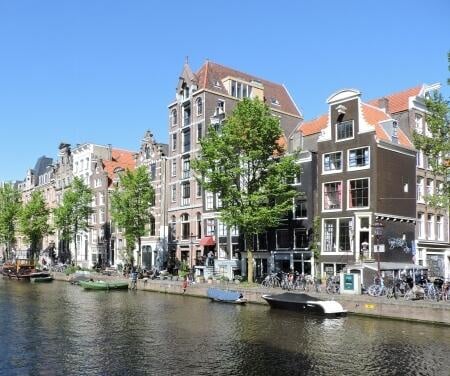 Case signorili lungo i canali di Amsterdam con barche ormeggiate in una giornata di sole.